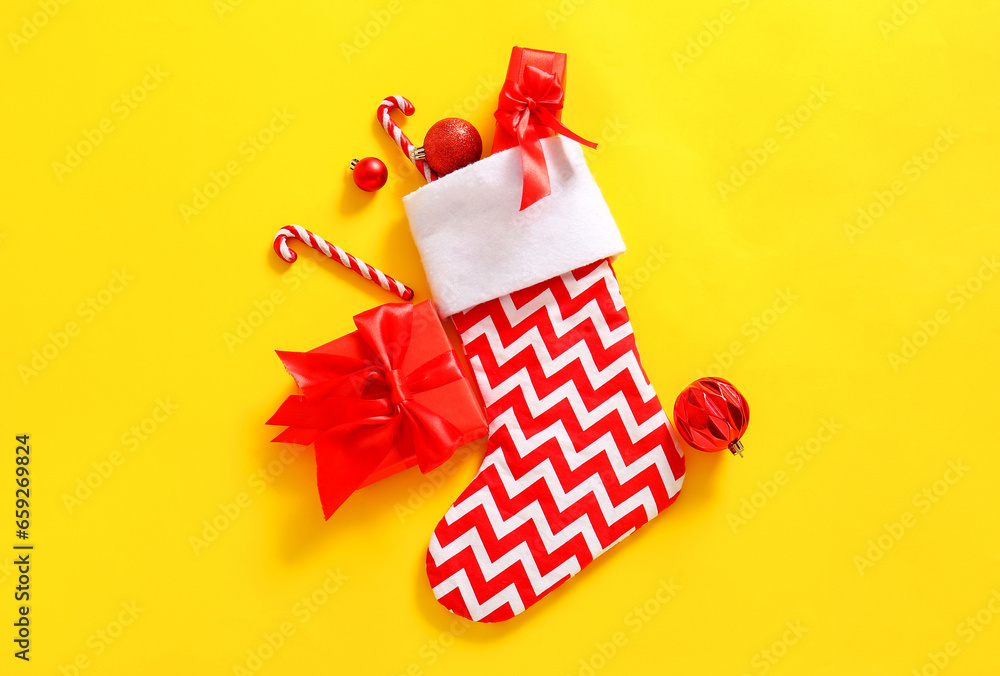 Christmas sock with balls, candy canes and gift boxes on yellow background