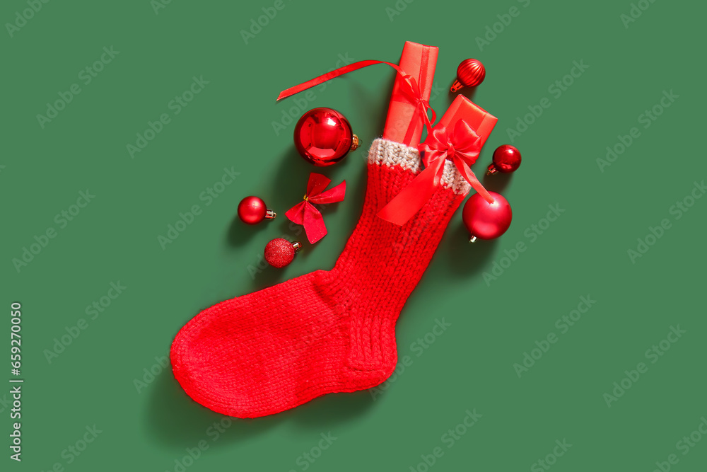 Christmas sock with balls and gift boxes on green background