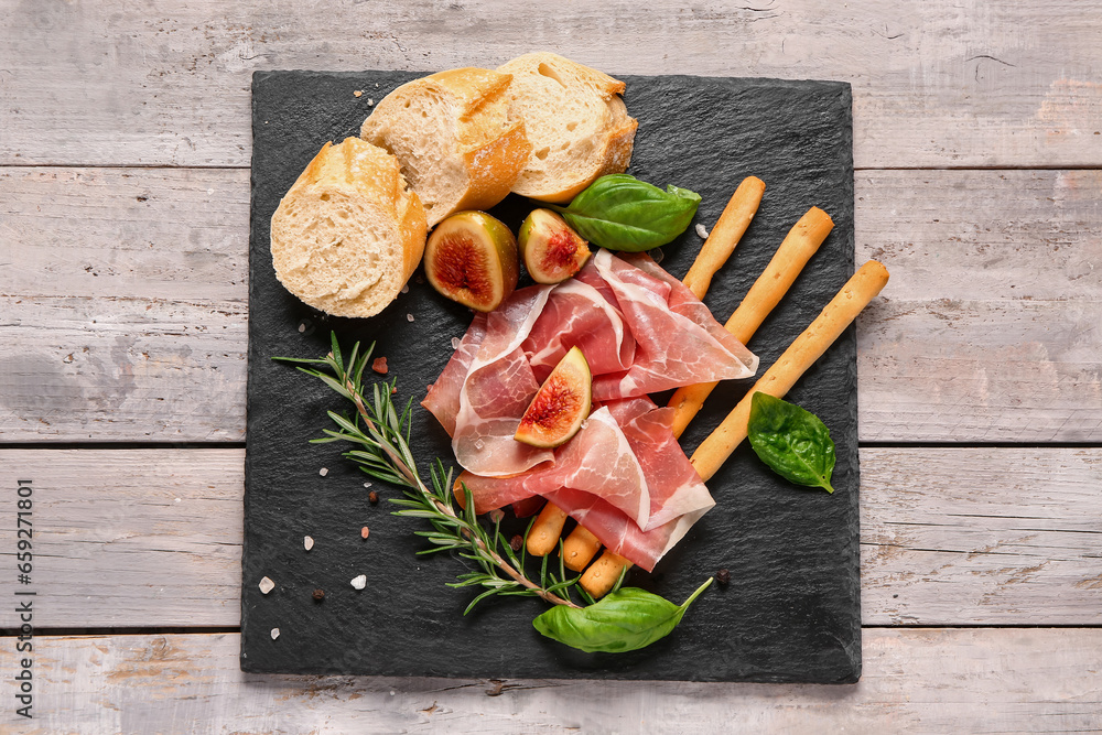 Board with slices of tasty prosciutto, basil, bread, Italian Grissini and figs on grey wooden background