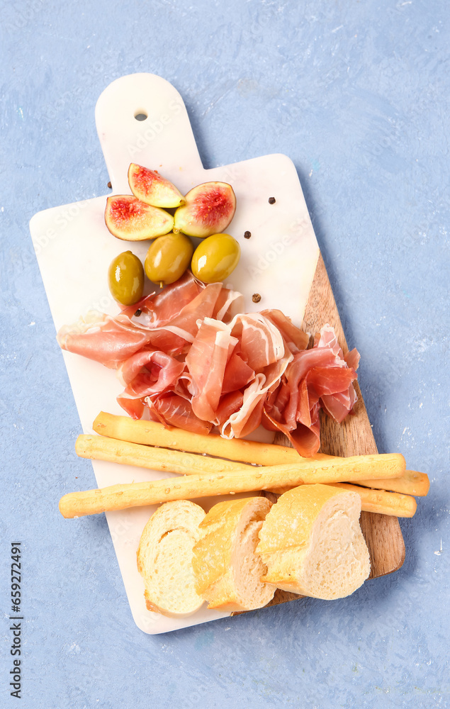 Board with slices of tasty prosciutto, Italian Grissini and bread on blue background