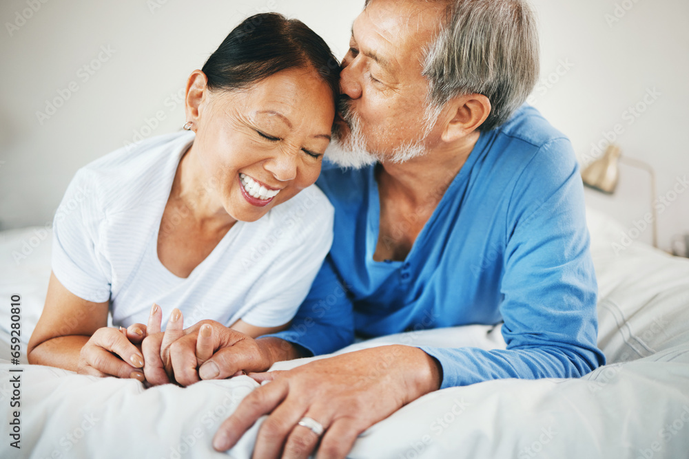 Love, holding hands and senior couple on bed for bonding, kissing and relaxing together at home. Happy, care and elderly Asian man and woman in retirement embracing for connection in bedroom at house