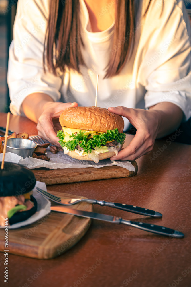 A young girl holding in female hands fast food burger, close up.