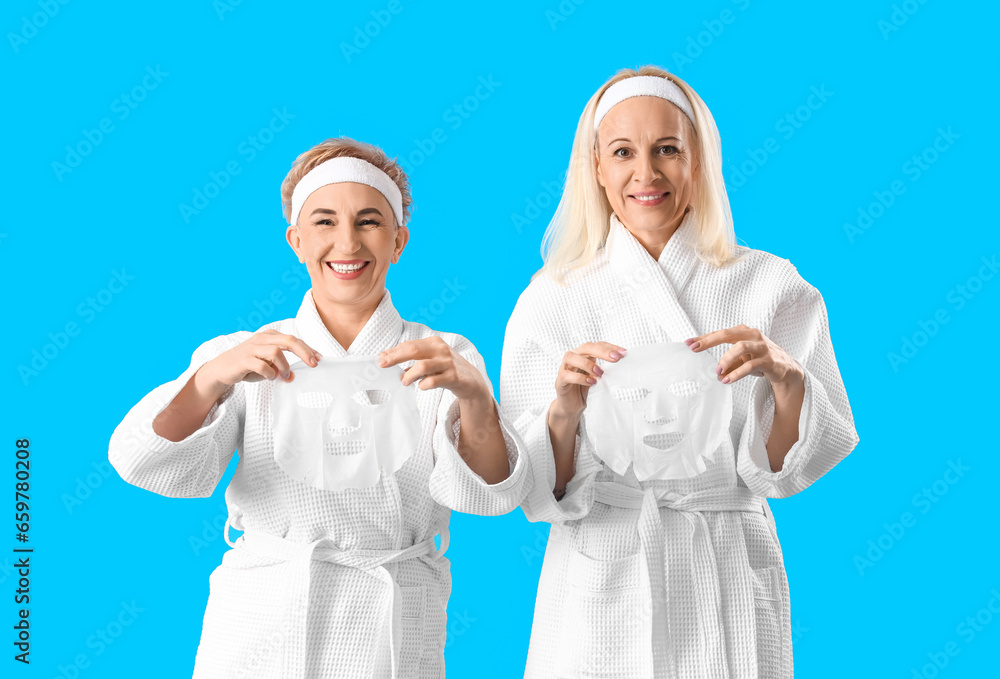 Mature women with facial masks on blue background