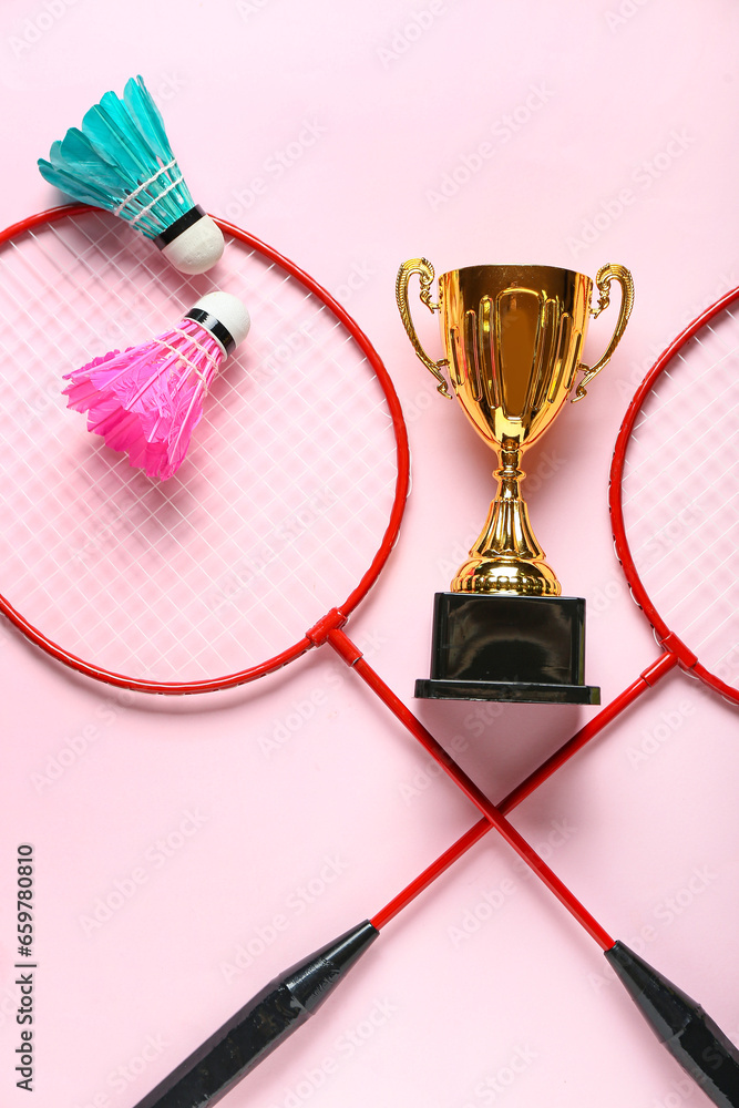 Gold cup with badminton rackets and shuttlecocks on pink background