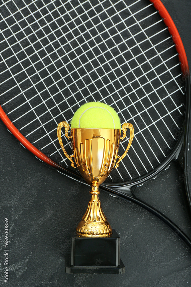 Gold cup with ball and tennis racket on dark background