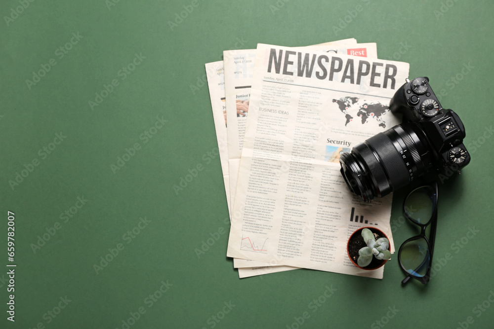 Newspapers with photo camera, eyeglasses and flowerpot on green background