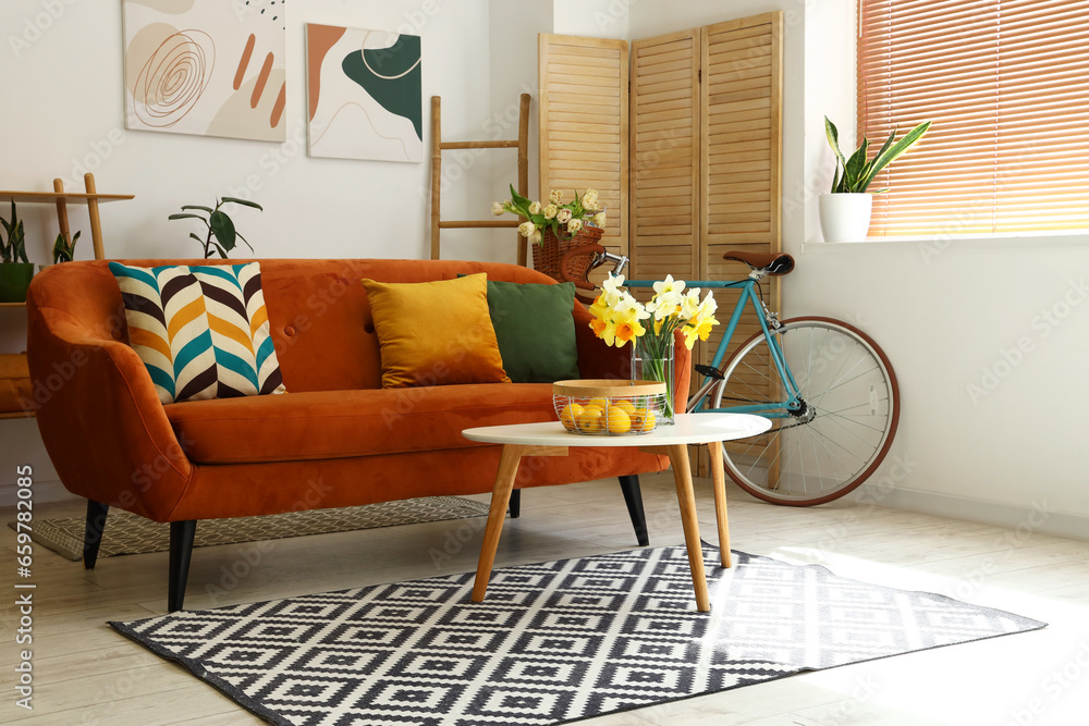 Interior of light living room with cozy brown sofa and narcissus flowers on coffee table