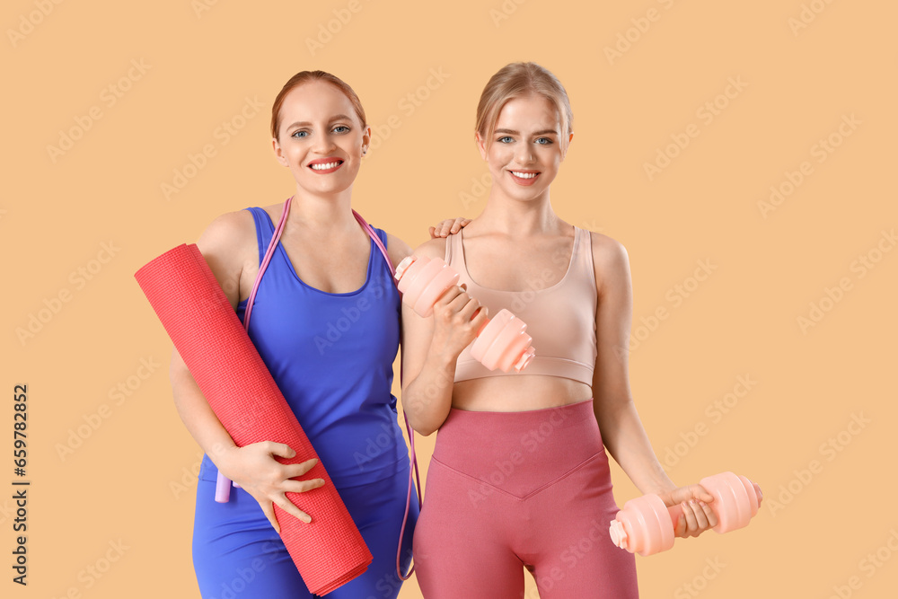 Sporty young women with yoga mat and dumbbells on beige background