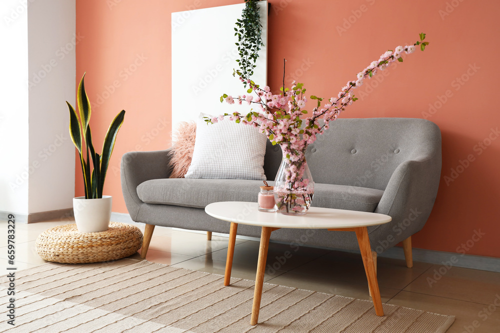 Interior of stylish living room with grey sofa and blooming sakura branches on coffee table