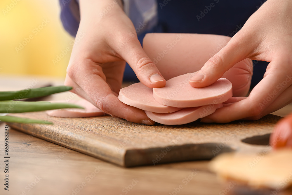 Woman holding boiled sausage at table in kitchen