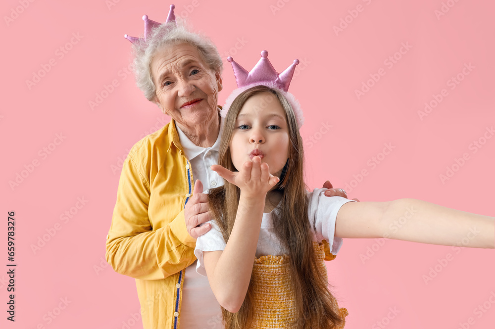 Little girl with her grandmother in crowns taking selfie on pink background