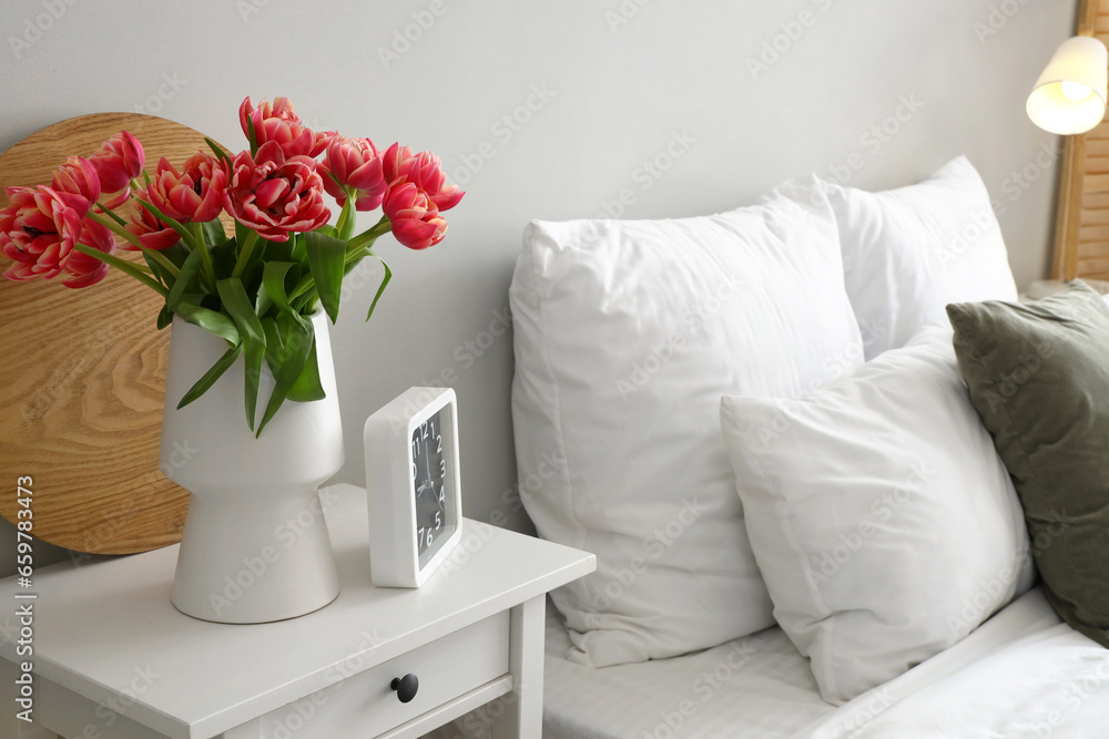 Vase with tulips and clock on table in bedroom