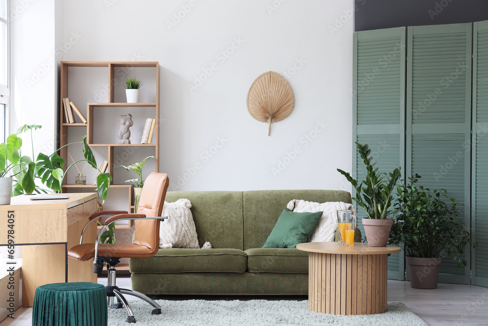 Interior of stylish living room with cozy green sofa and comfortable workplace near big window