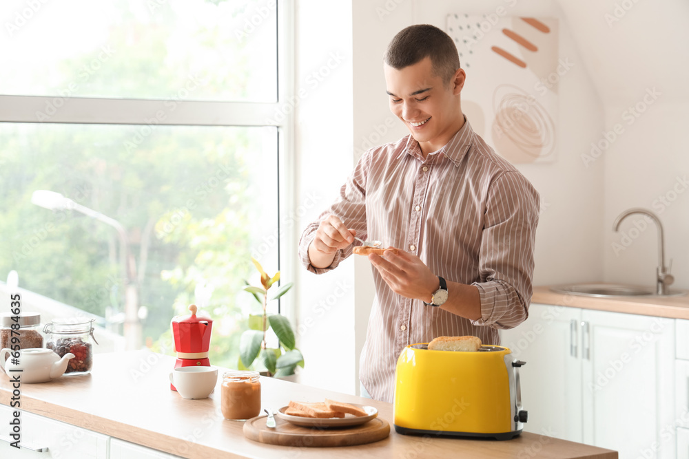 Young man making toast with tasty nut butter in kitchen