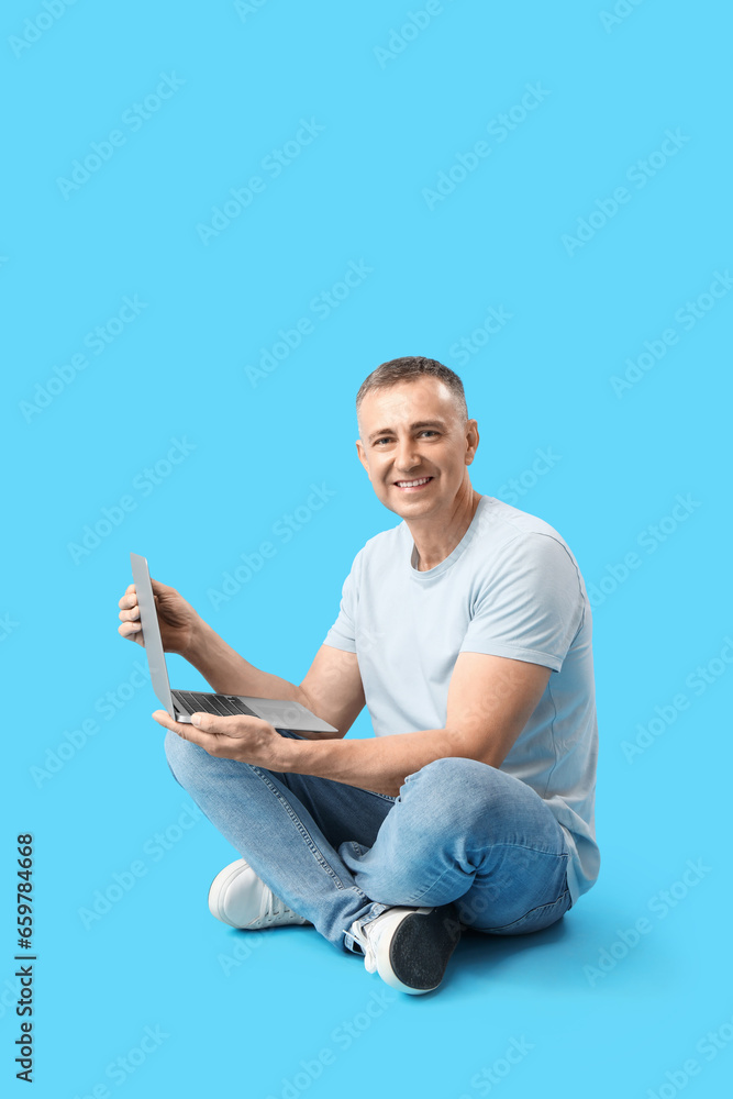 Mature male programmer with laptop sitting on blue background