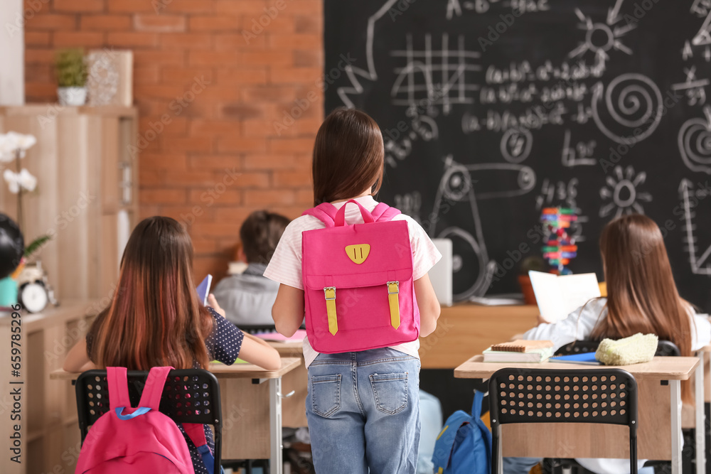 Little girl with backpack in classroom, back view