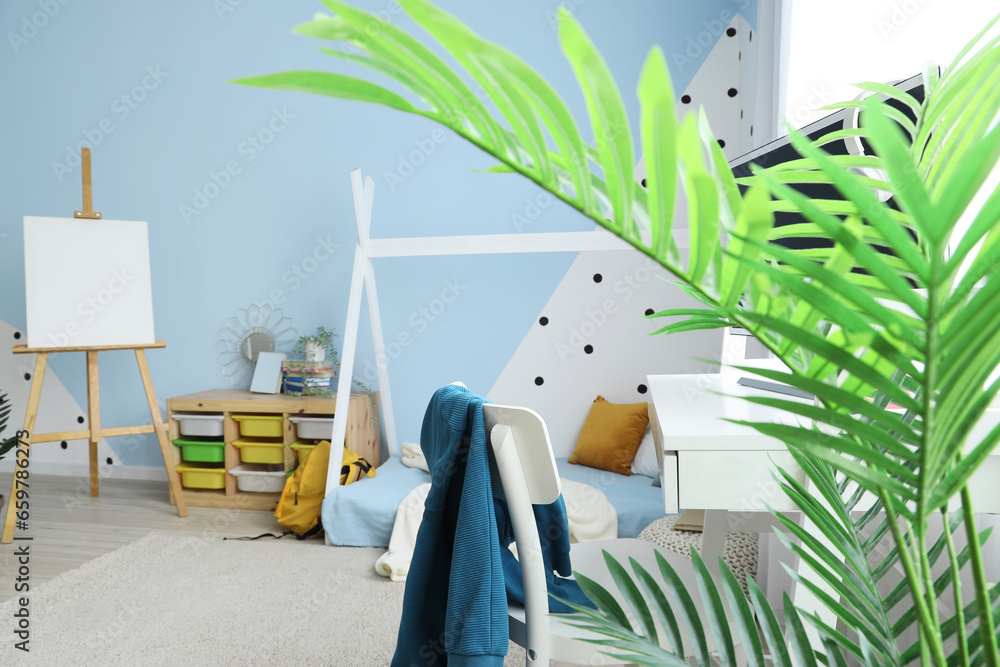 Interior of childrens bedroom with cozy bed, easel and houseplant