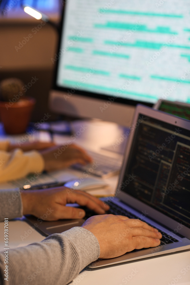 Male programmer working with laptop in office at night, closeup