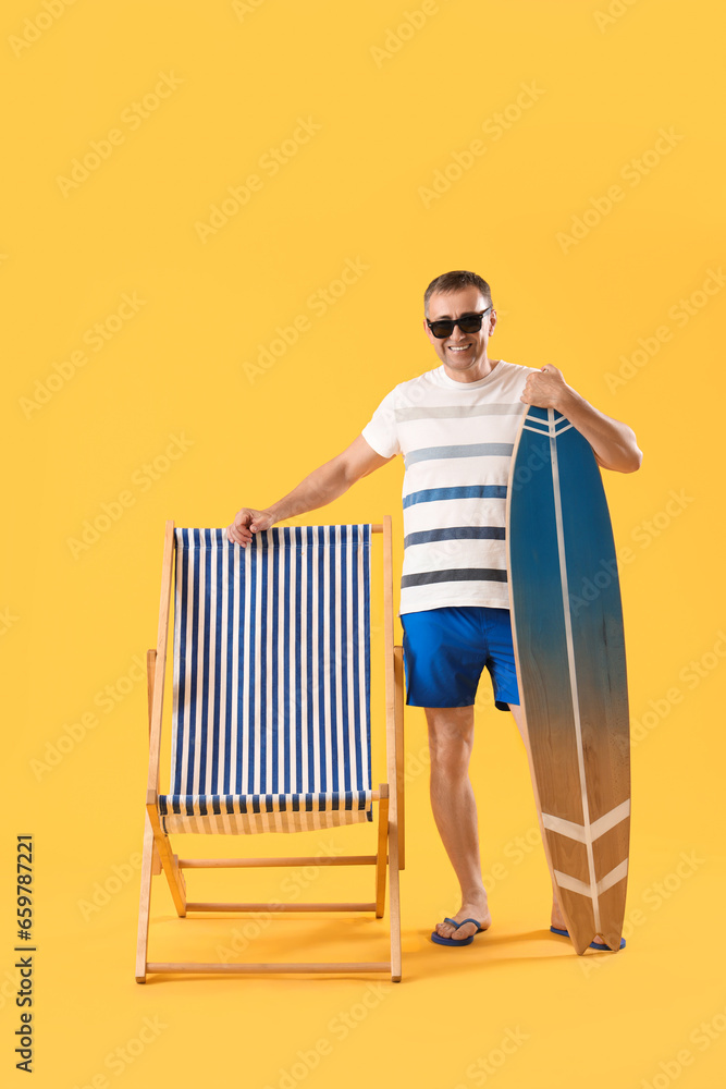 Mature man with surfboard and deck chair on yellow background