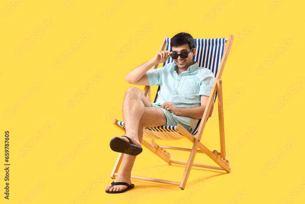 Young man relaxing in deck chair on yellow background