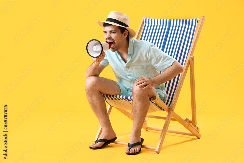 Young man with megaphone shouting in deck chair on yellow background