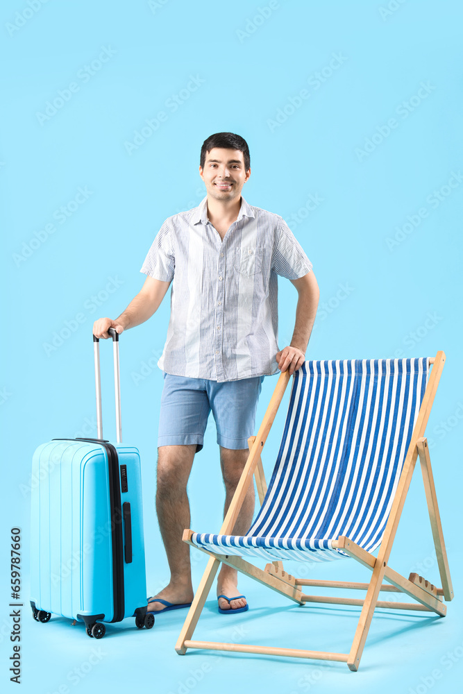 Young man with suitcase and deck chair on blue background