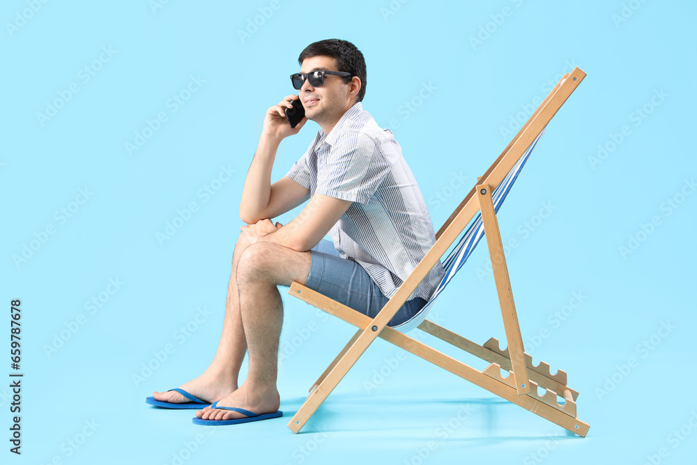 Young man talking by mobile phone in deck chair on blue background