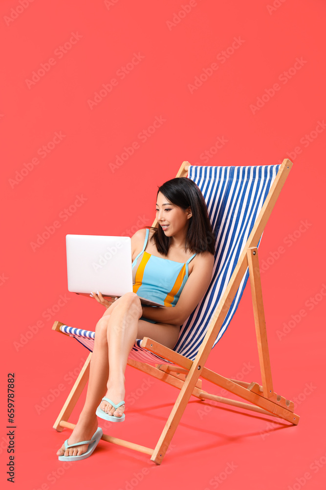 Beautiful Asian woman using laptop in deck chair on red background