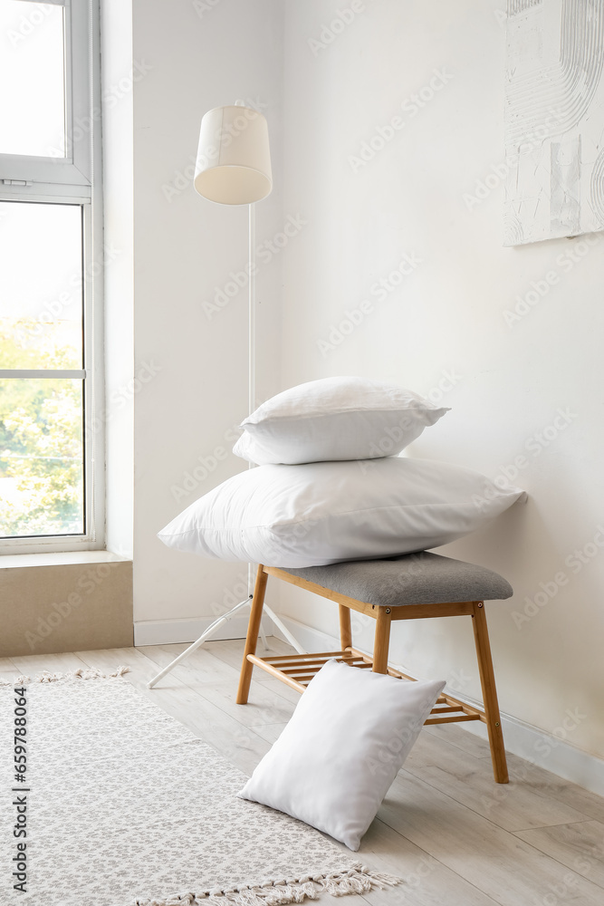 Grey bench with pillows and standard lamp near white wall