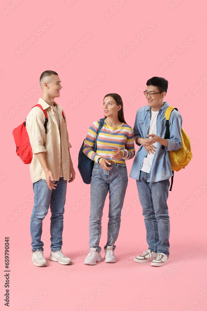 Happy students with backpacks on pink background