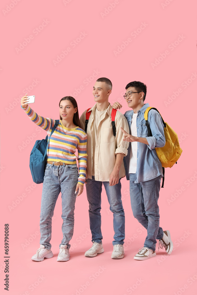 Happy students with backpacks taking selfie on pink background