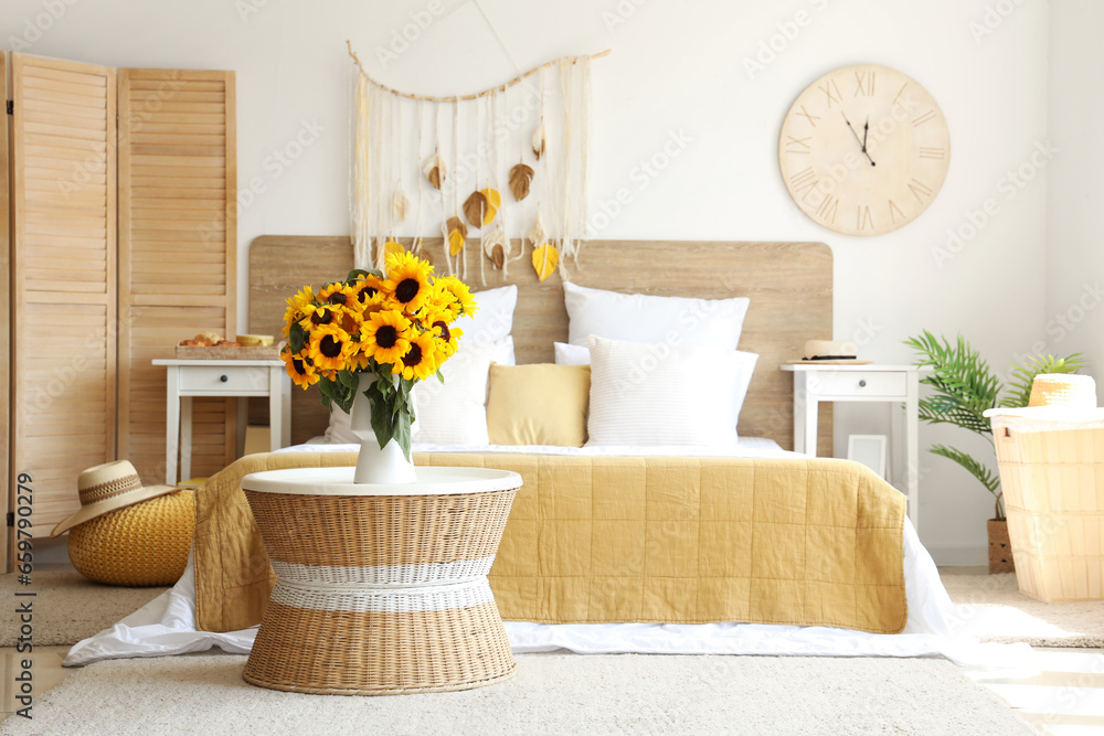 Interior of light bedroom with sunflowers in vase on table