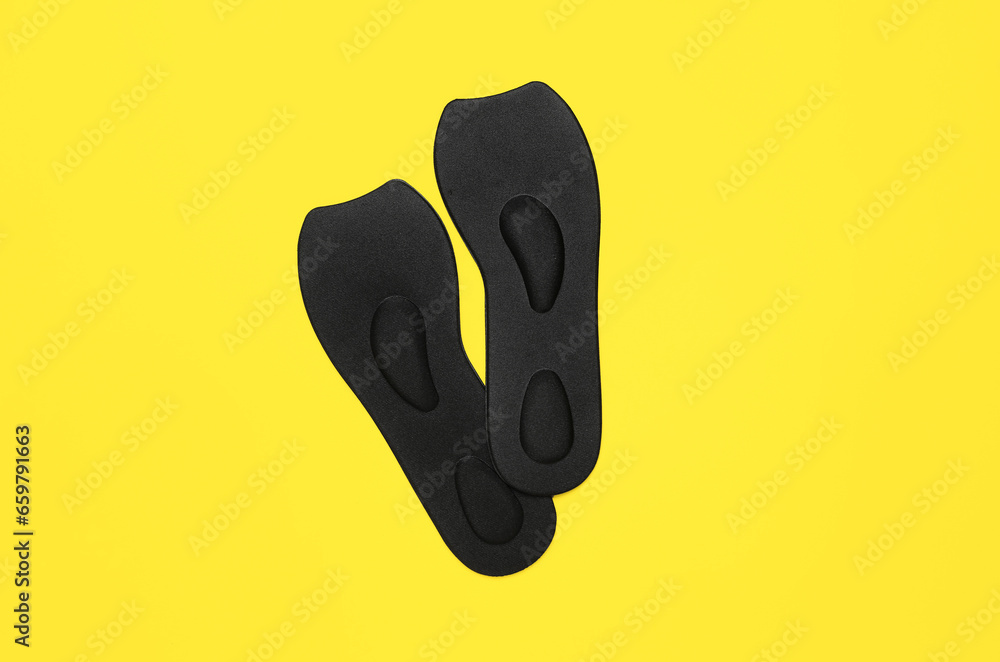 Pair of black orthopedic insoles on yellow background