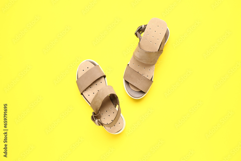 Pair of stylish female sandals with orthopedic insoles on yellow background