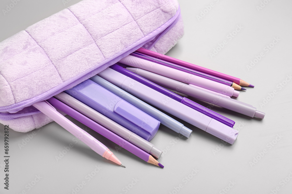 Purple pencil case with school stationery on grey background, closeup