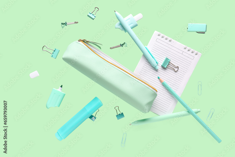 Flying pencil case and school stationery on green background