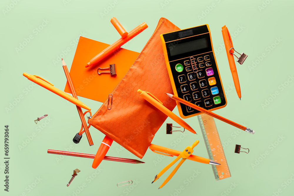 Flying orange pencil case and school stationery on green background