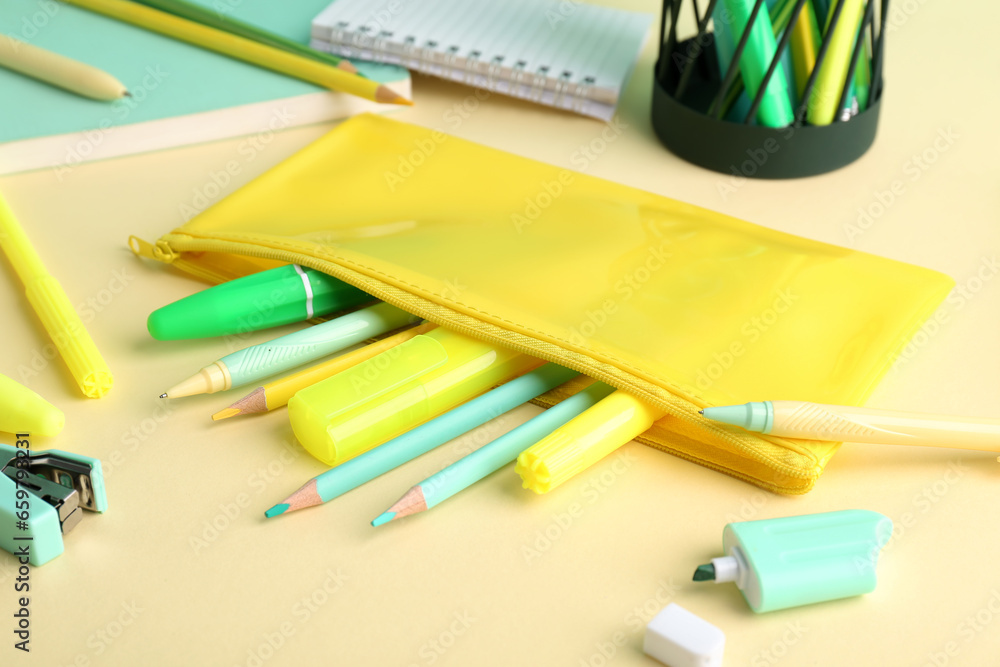 Yellow pencil case with school stationery on beige background, closeup