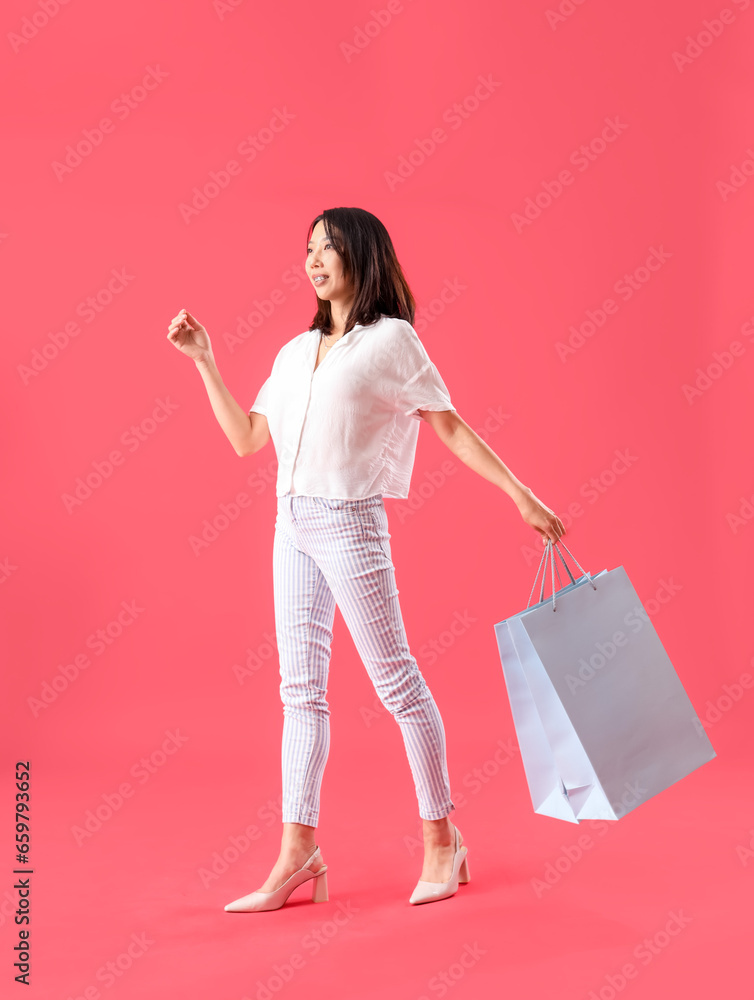 Beautiful stylish young Asian woman with shopping bags on red background