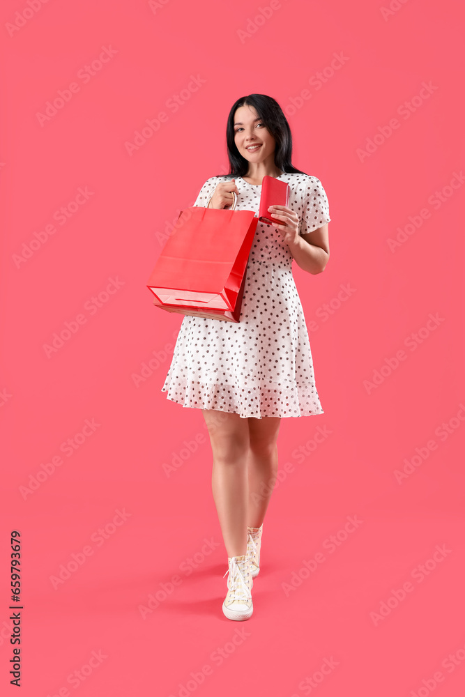 Portrait of beautiful young woman with shopping bag and purse on red background