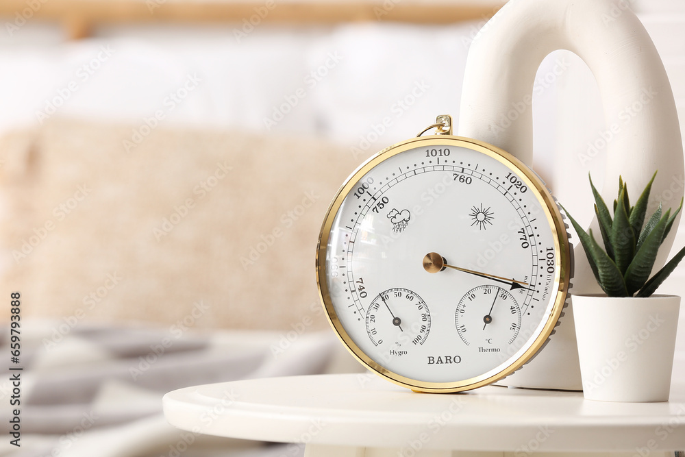 Aneroid barometer and small houseplant on table in room, closeup