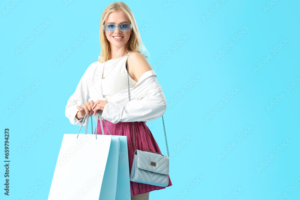 Beautiful young woman in sunglasses with shopping bags on blue background