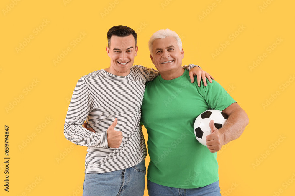 Young man with his father and soccer ball hugging on yellow background