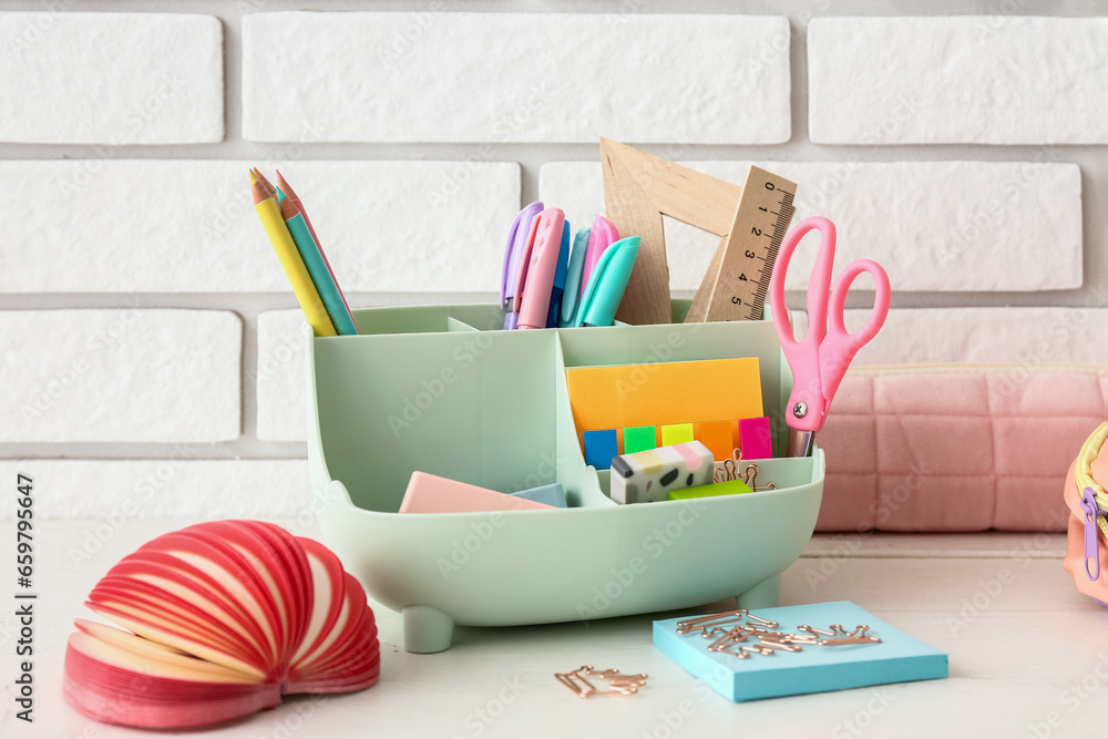 Holder with different stationery on light wooden desk, closeup