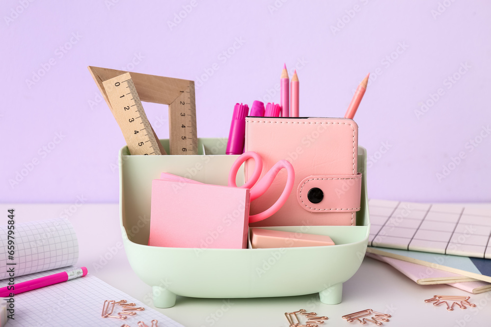 Holder with different stationery and notebooks on light desk, closeup