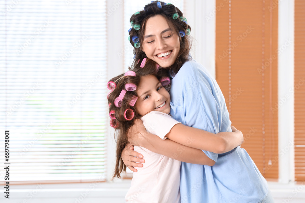 Little girl and her mother with hair curlers hugging at home