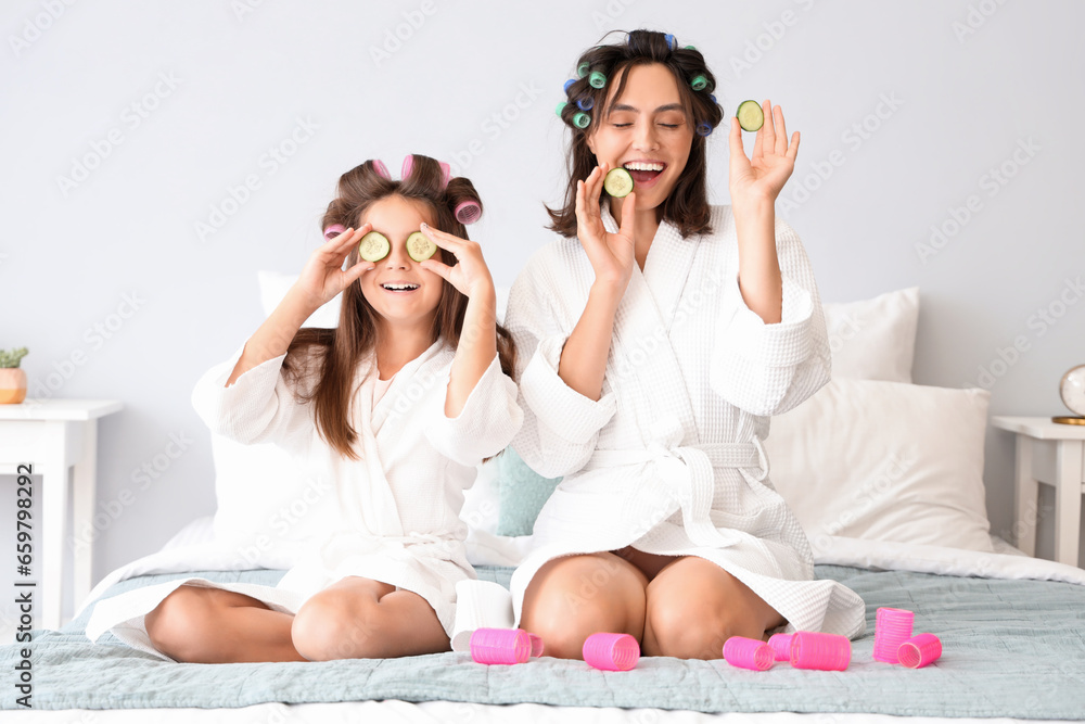 Little girl and her mother with cucumber slices curling hair in bedroom