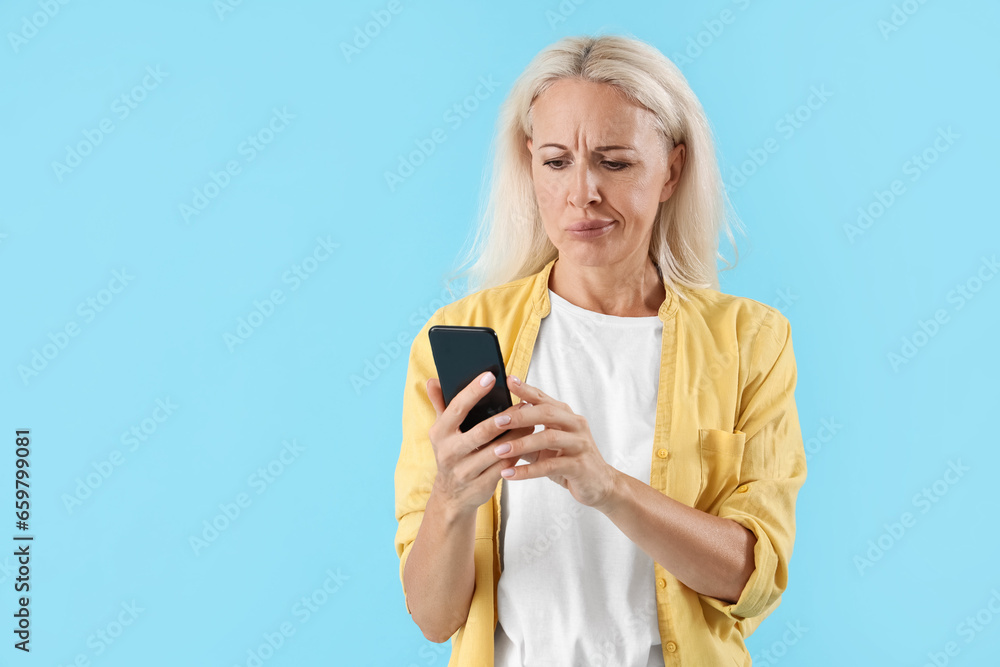 Thoughtful mature woman using mobile phone on blue background