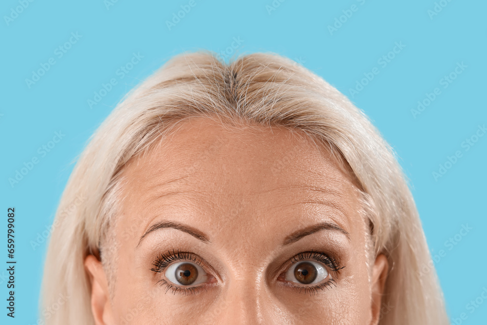 Thoughtful mature woman on blue background, closeup