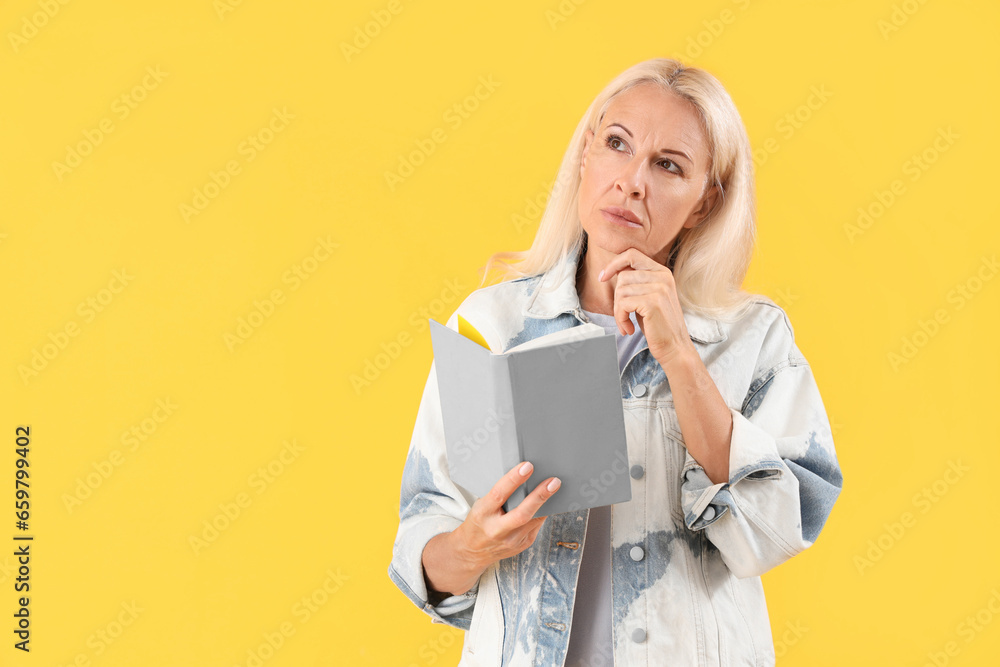 Thoughtful mature woman with book on yellow background